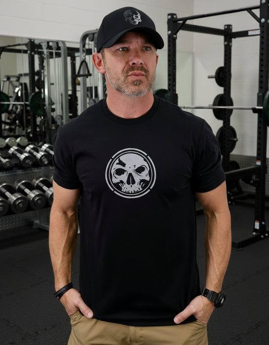 Man wearing a black t-shirt with a skull logo and a cap on a white background
