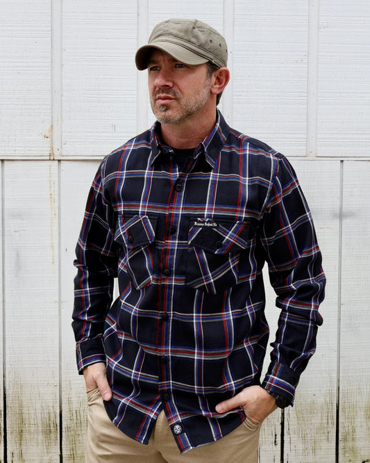 Man wearing a plaid shirt and cap against a white wooden background