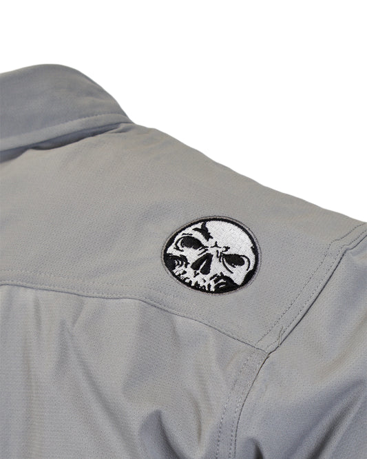 Close-up of embroidered skull shoulder patch on gray micro-perforated stretch button-up.