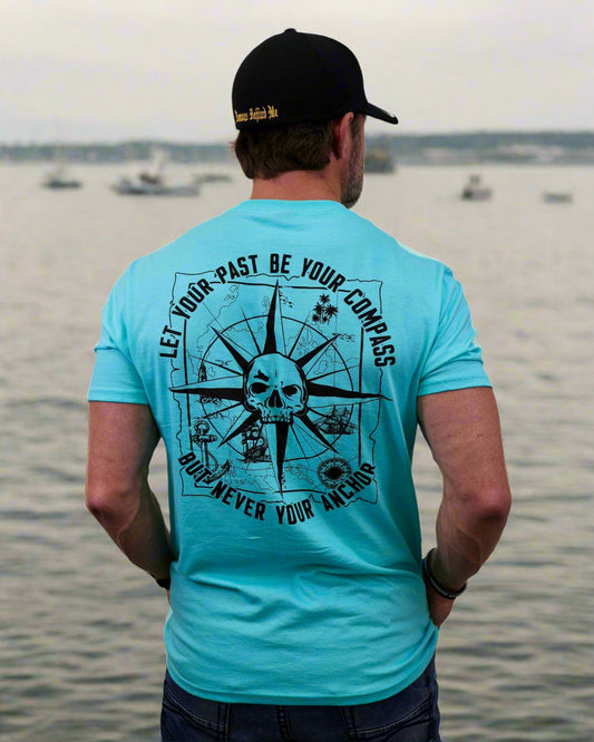 Person wearing a turquoise t-shirt with a skull and compass design on the back, standing against a white background.