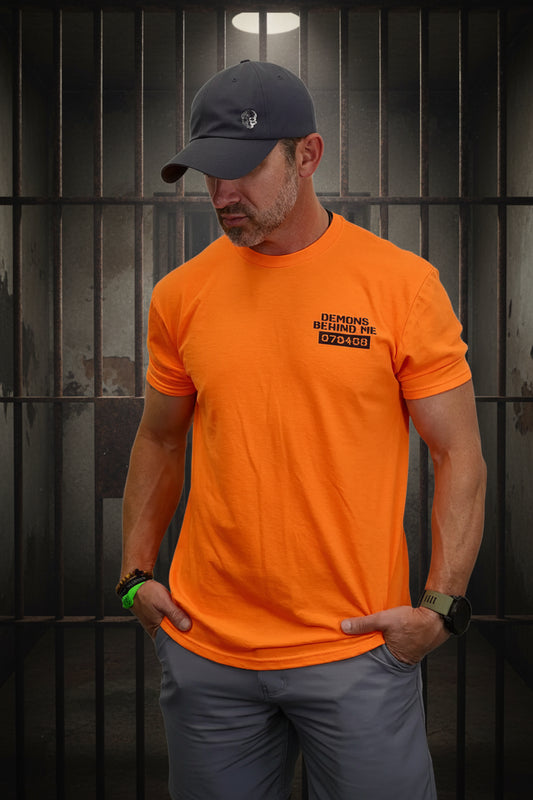 Man wearing an orange t-shirt with a logo and text, standing against a white background