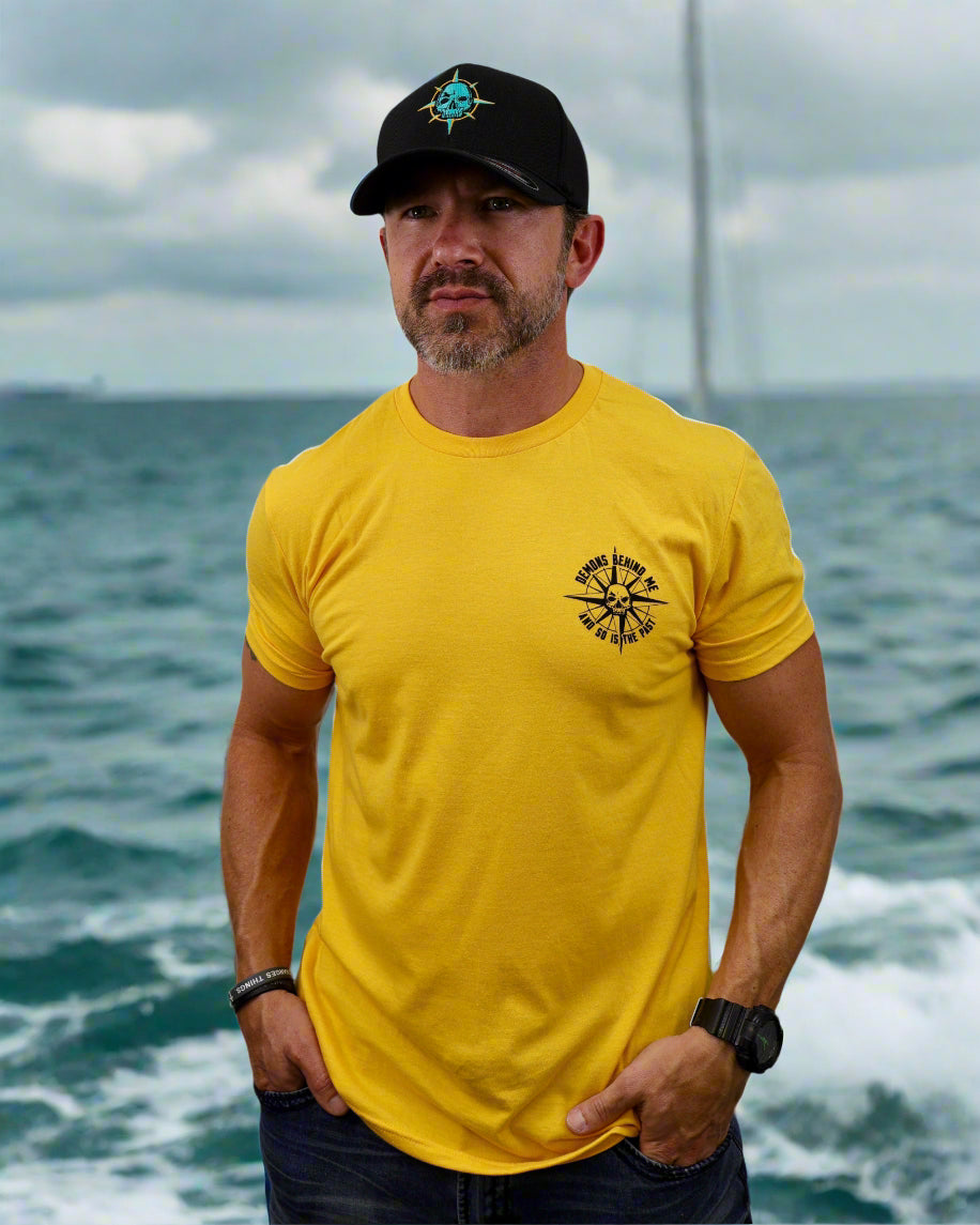 Man wearing a yellow t-shirt with a logo and a black cap on a white background