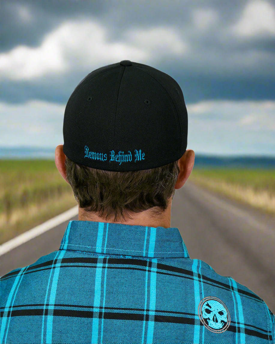Person wearing a black cap with 'Revenant Behind Me' text and a blue plaid shirt with a logo.