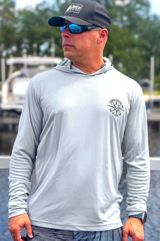 Man wearing a gray long-sleeve shirt with a logo, black cap, and sunglasses outdoors.