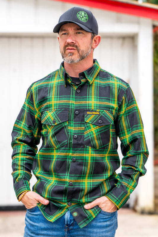 Man wearing a green and black plaid shirt with a cap, standing outdoors.