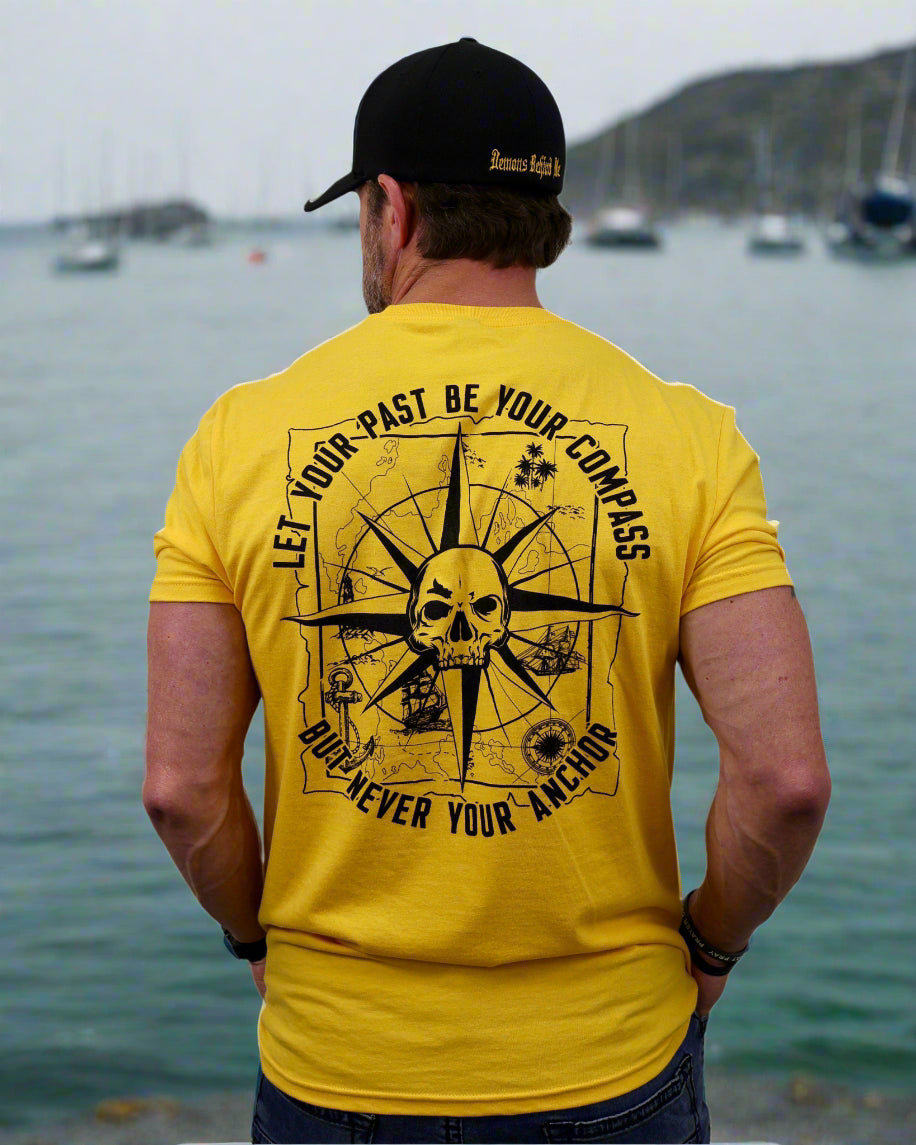 Man wearing a yellow t-shirt with a compass and skull design, black cap, on a white background