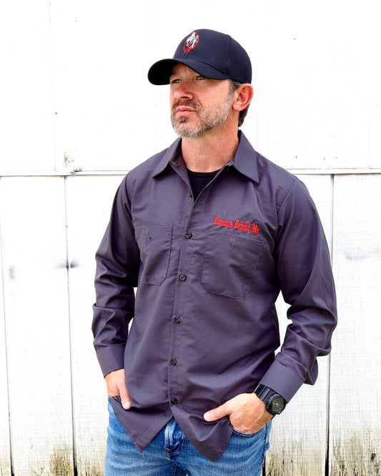 Man wearing a dark gray shirt with a logo and text, standing against a white wooden fence.