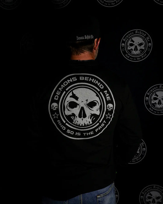 Man wearing “The Ghost” reflective long-sleeve tee at night, back view with illuminated skull graphic