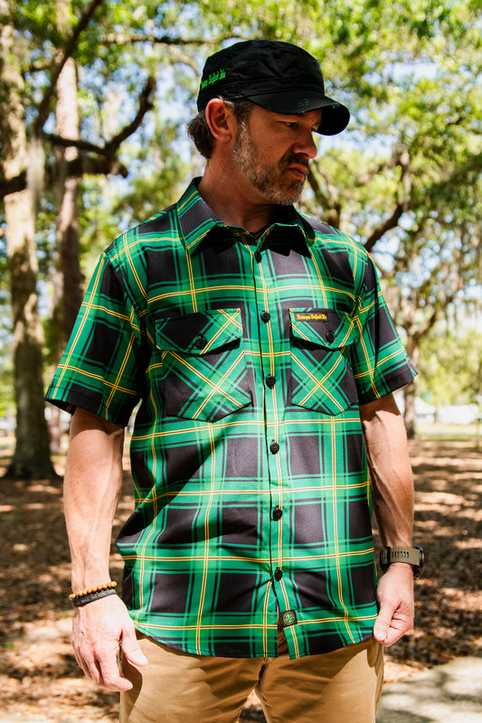Man at the park wearing bold green and black button up shirt with a black Demons Behind Me hat.