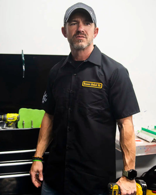 Man wearing a black shirt with a logo, holding tools in a workshop setting