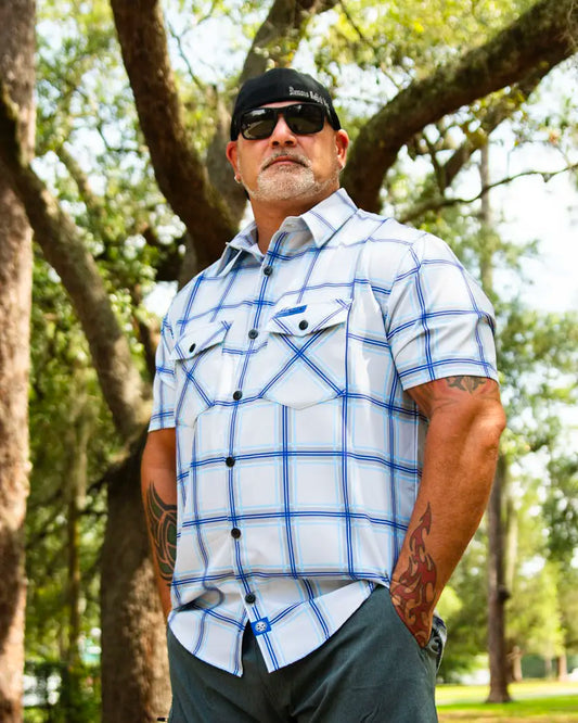 Man wearing blue and gray plaid button up shirt standing in a park