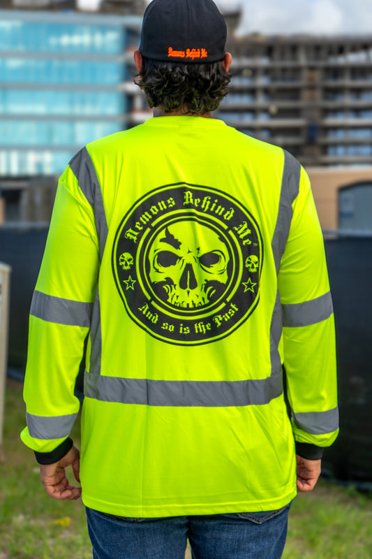 Person wearing a bright yellow safety jacket with a skull design on the back, standing outdoors.