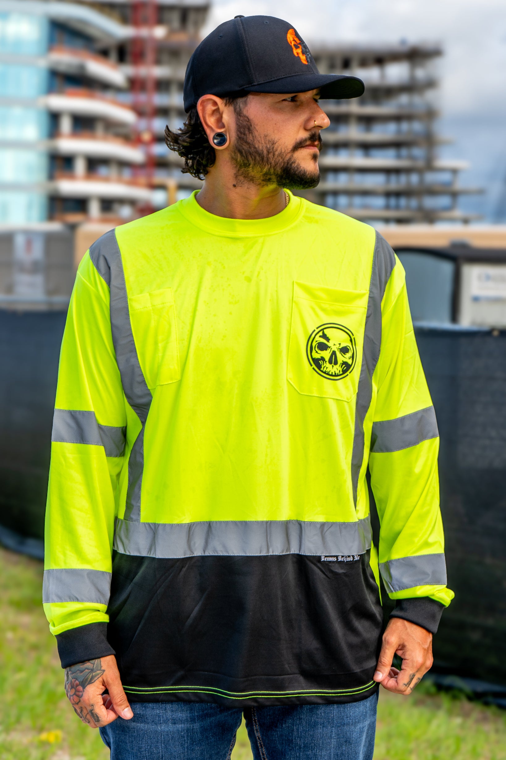 Person wearing a high-visibility safety shirt with reflective stripes and a logo, standing outdoors.